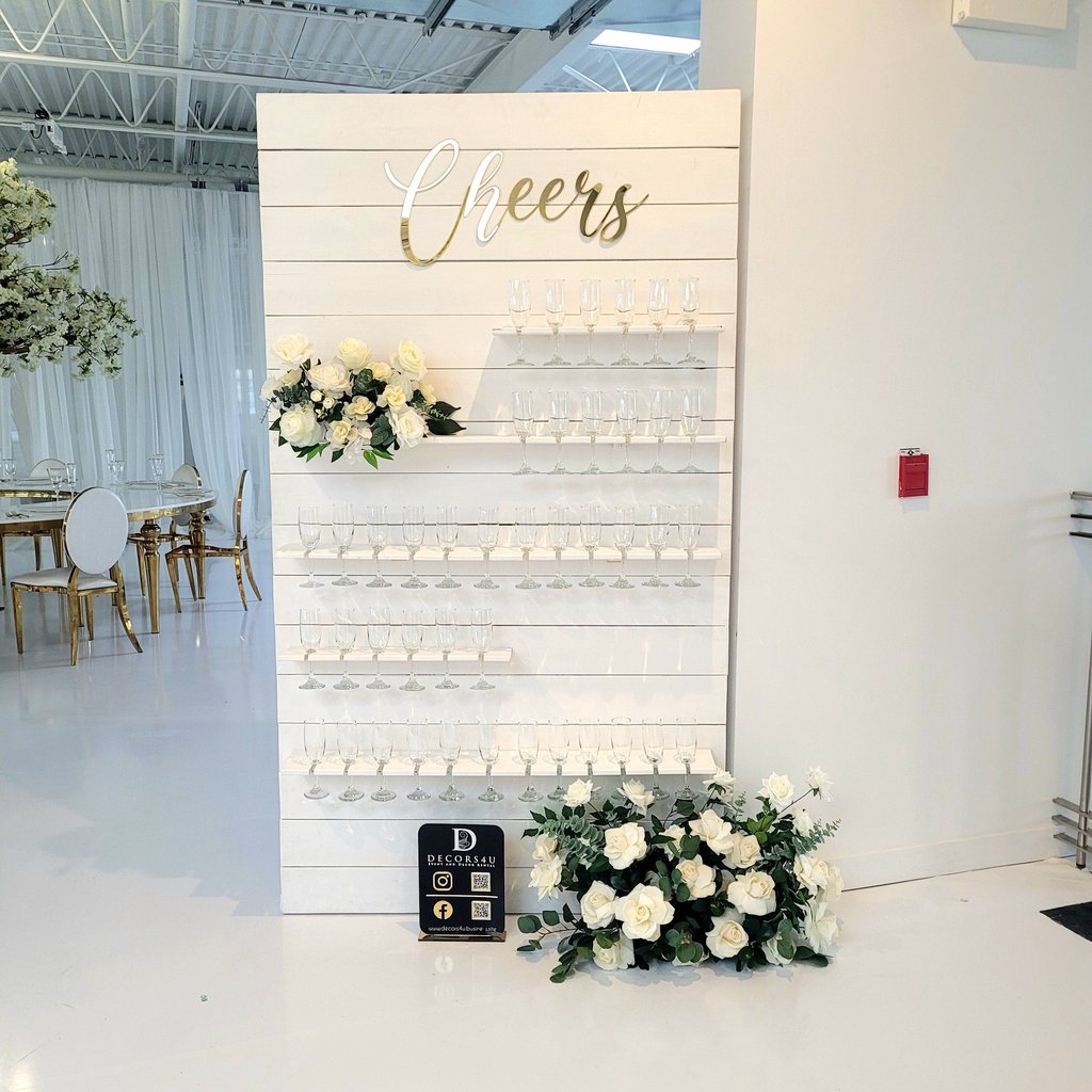 White champagne with white roses and greenery flowers and a sign that says cheers