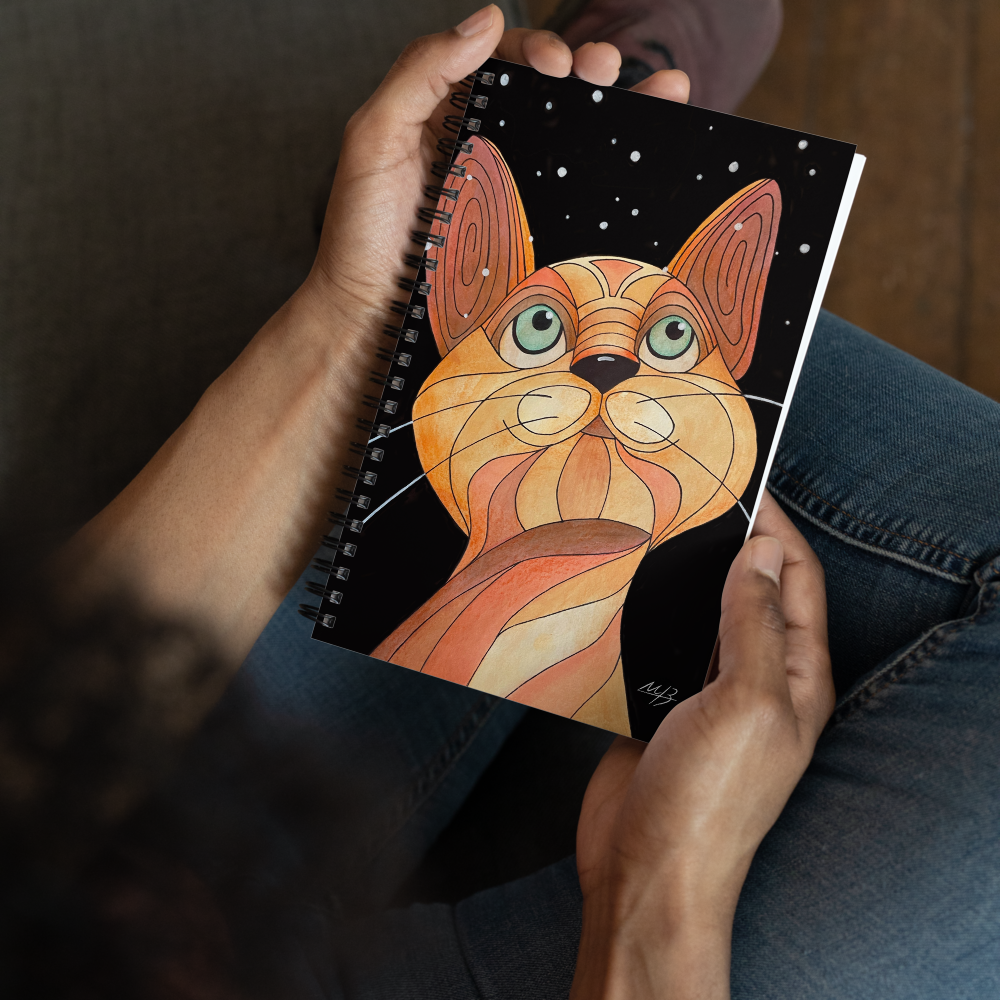 Person holding a spiral notebook featuring a whimsical cat art illustration by Mara Branco.