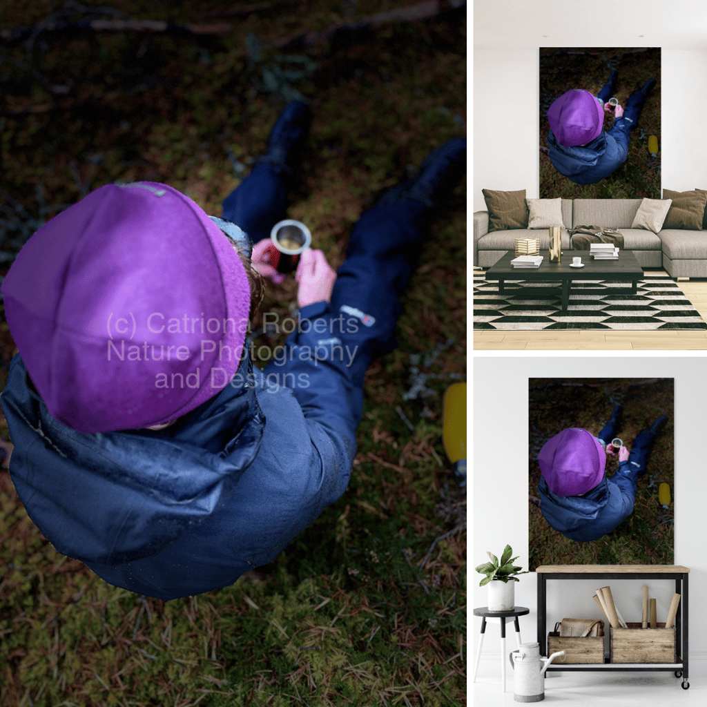 a person wearing outdoor clothes sitting on moss holding a mug with liquid in it 