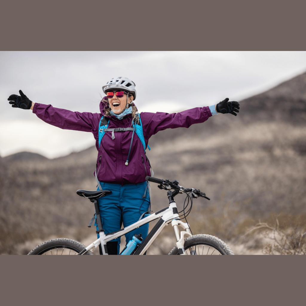 a young woman standing in front of her mountain bike with her arms outstretched 