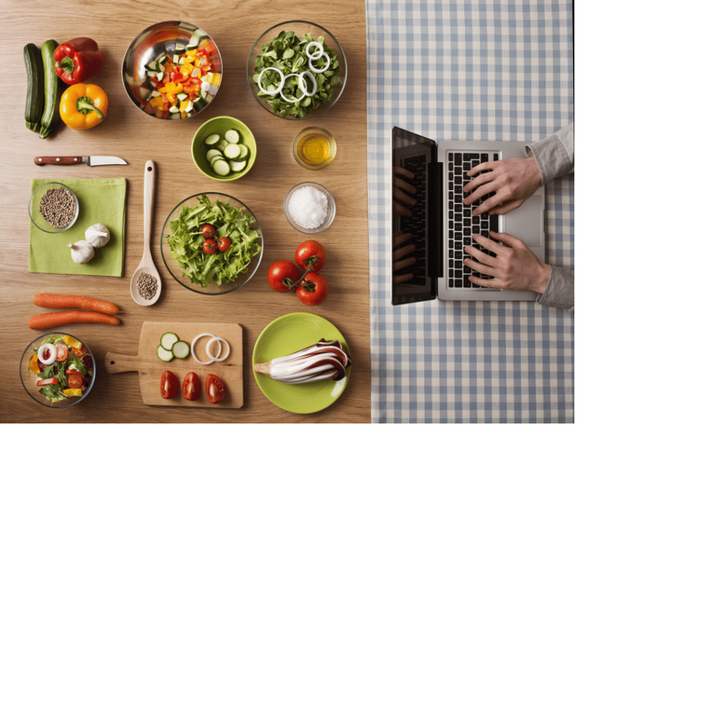 Person typing on laptop at other end of table that displays many dishes/ingredients