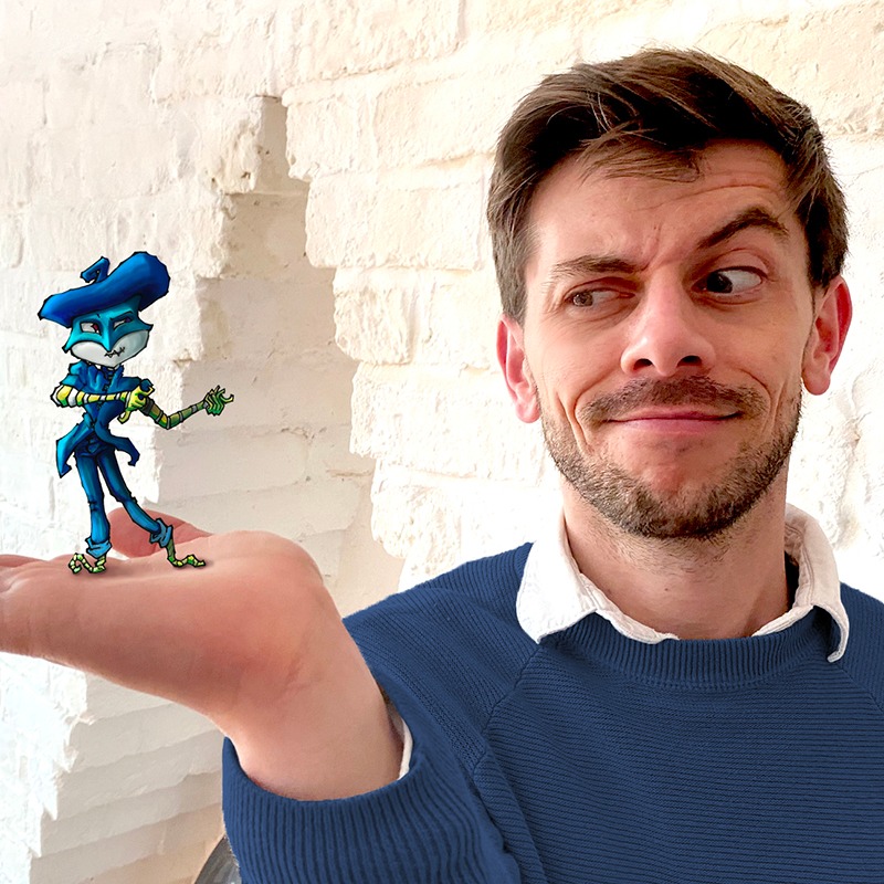 Young handsome gay male artist wearing a blue jumper holds one of his fantasy art figures.