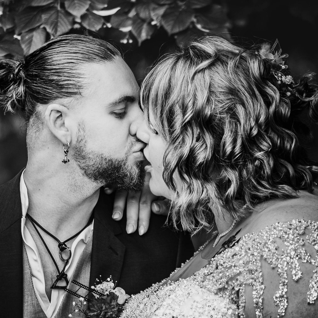 Une photo de mariage en noir et blanc montrant les mariés échangeant un baiser intime en extérieur.