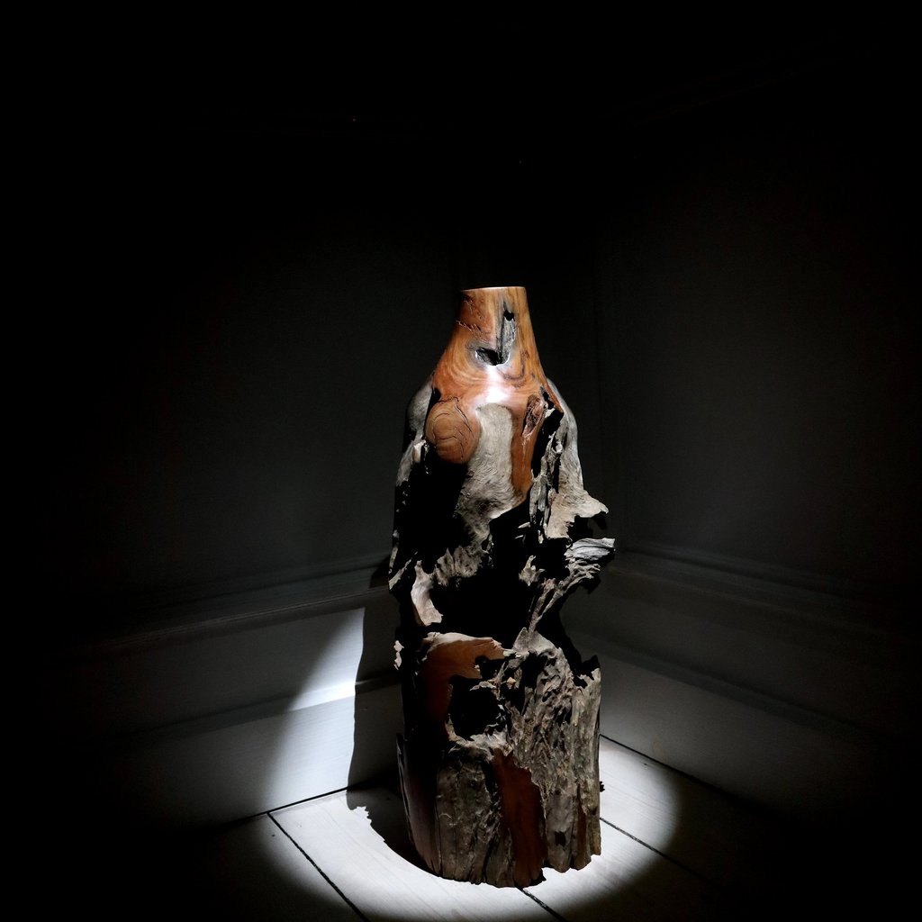 Rustic hand-carved natural wood sculpture spotlighted in a dark room as a piece of fine art decor.