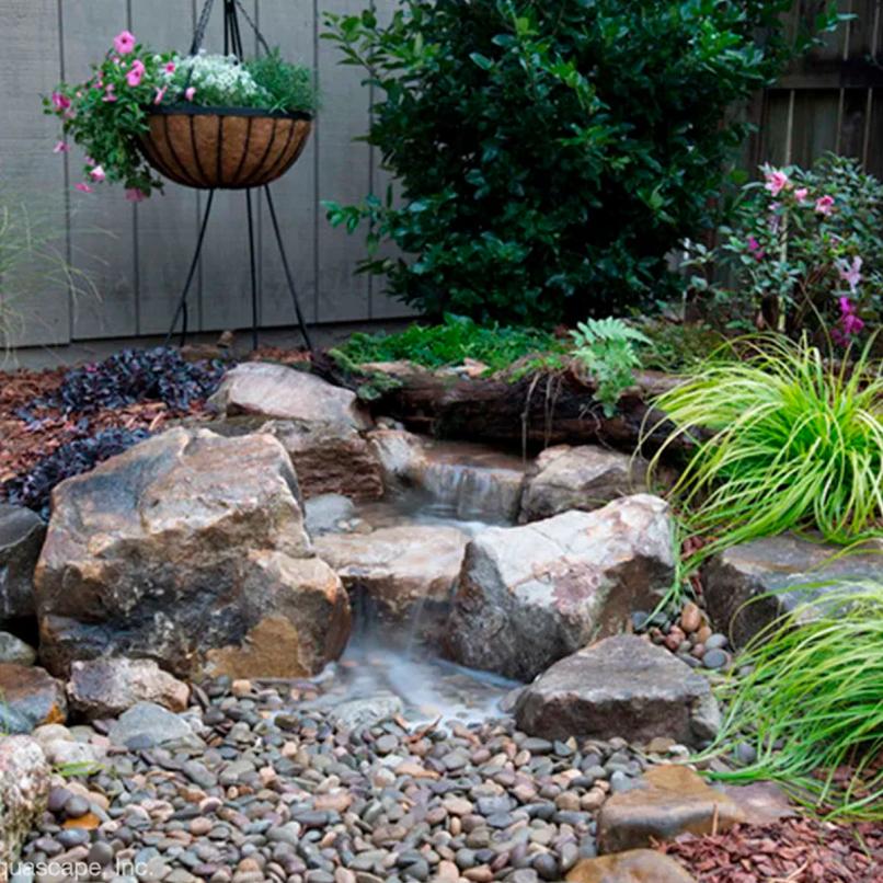 Backyard garden waterfall surrounded by rocks and plants
