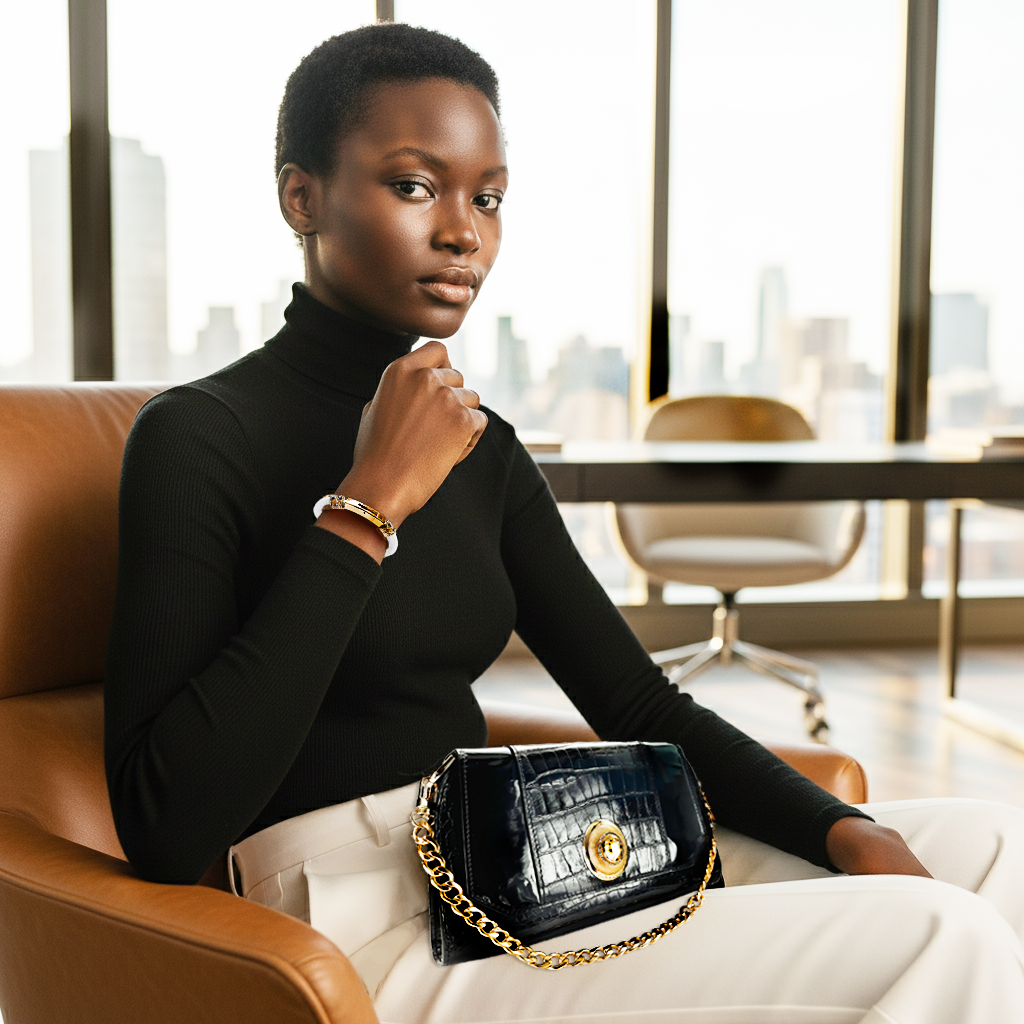 A stylish woman in a black turtleneck holds a black croc-effect handbag with a gold chain.