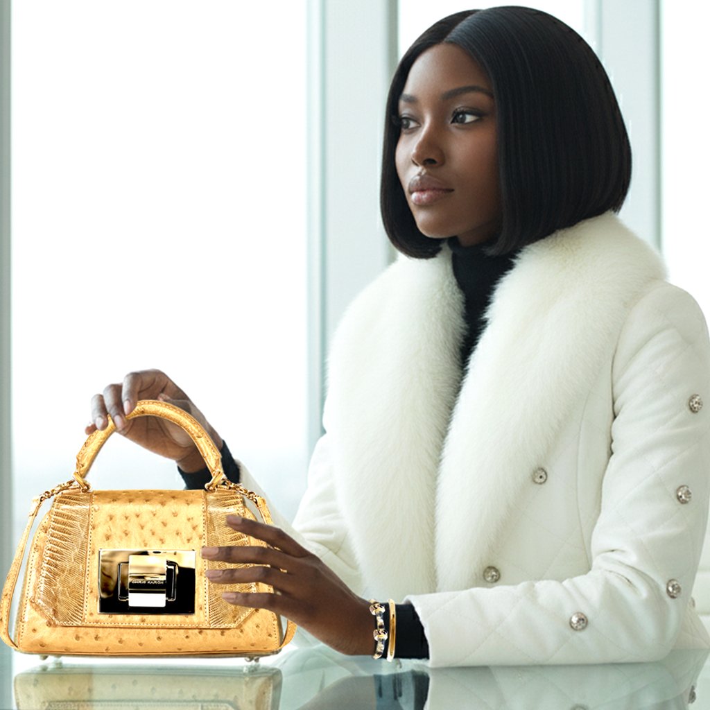 Elegant woman in white fur collar jacket holding a luxury gold ostrich leather handbag.