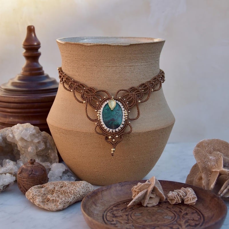 Collar de macramé hecho a mano con piedra verde exhibido sobre jarrón de cerámica y cristales natura