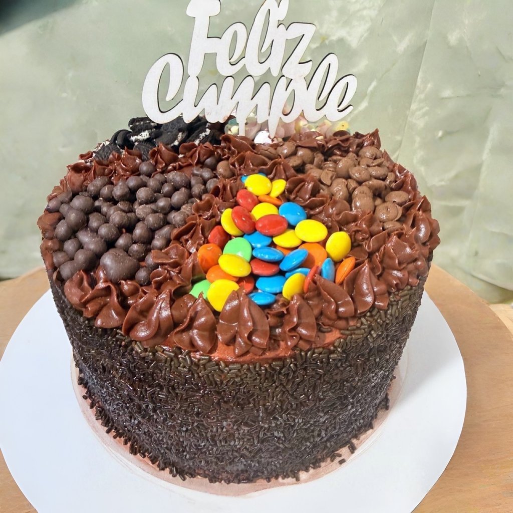 Pastel de cumpleaños de chocolate con chispas, caramelos y un adorno de pastel Feliz Cumple.