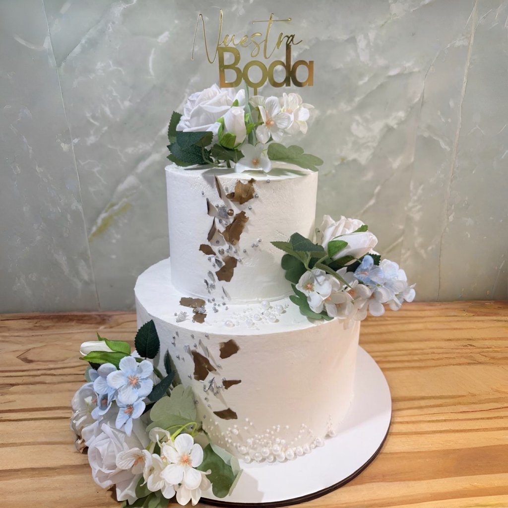 Elegante pastel de bodas blanco de dos niveles decorado con pan de oro, flores blancas y un adorno d