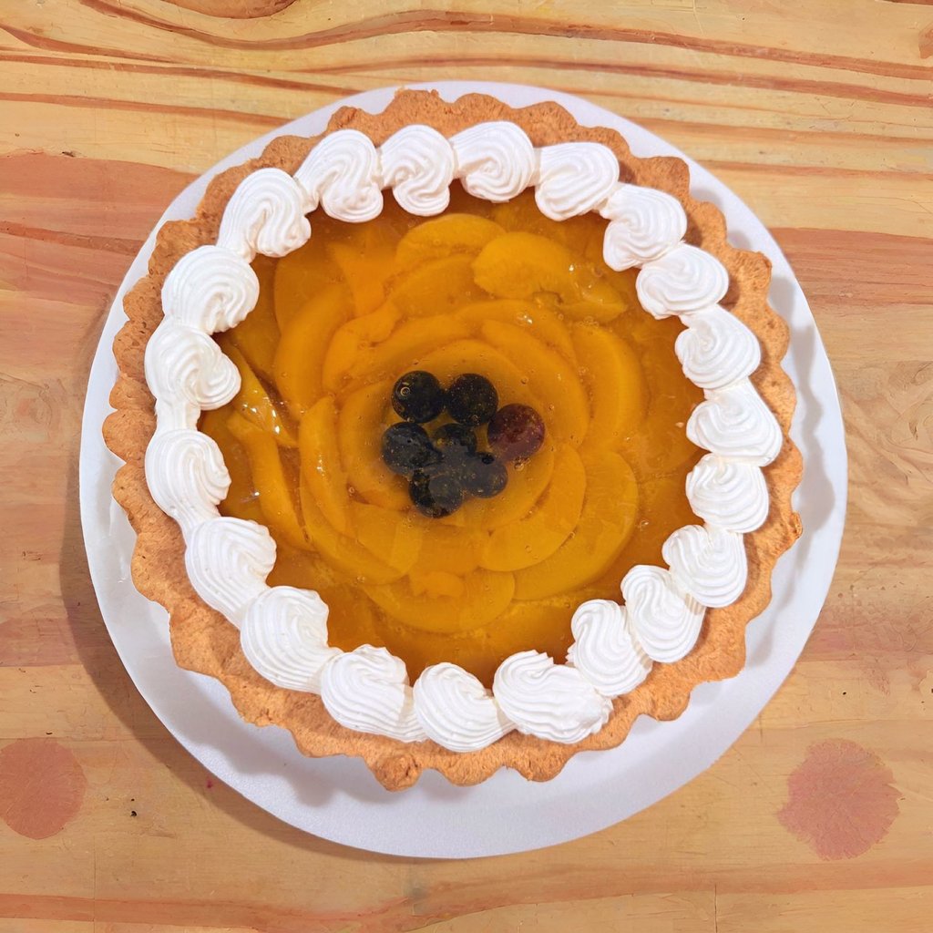 Tarta de melocotón fresco con fruta glaseada, borde de crema batida y arándanos sobre una mesa de ma