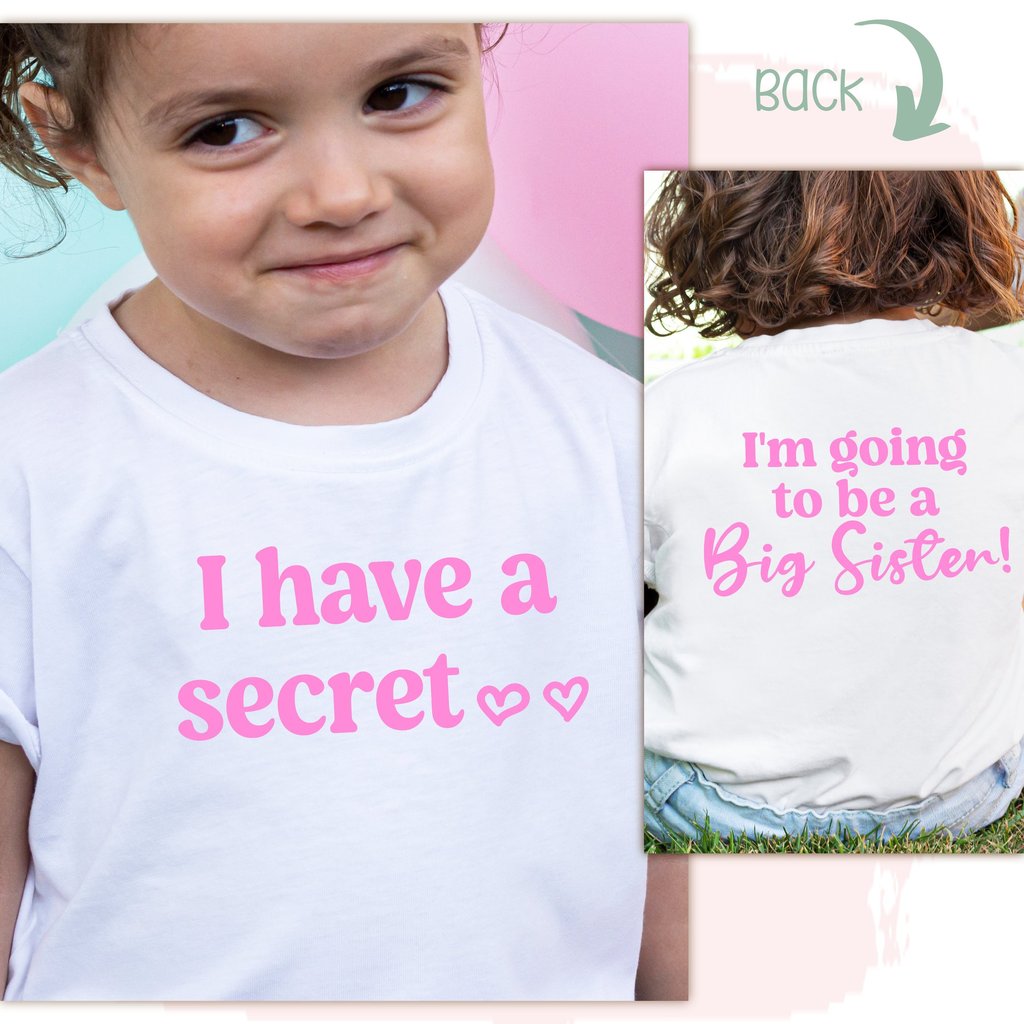 little girl wearing a white shirt with pink letters & "I have a secret I'm going to be a Big Sister"