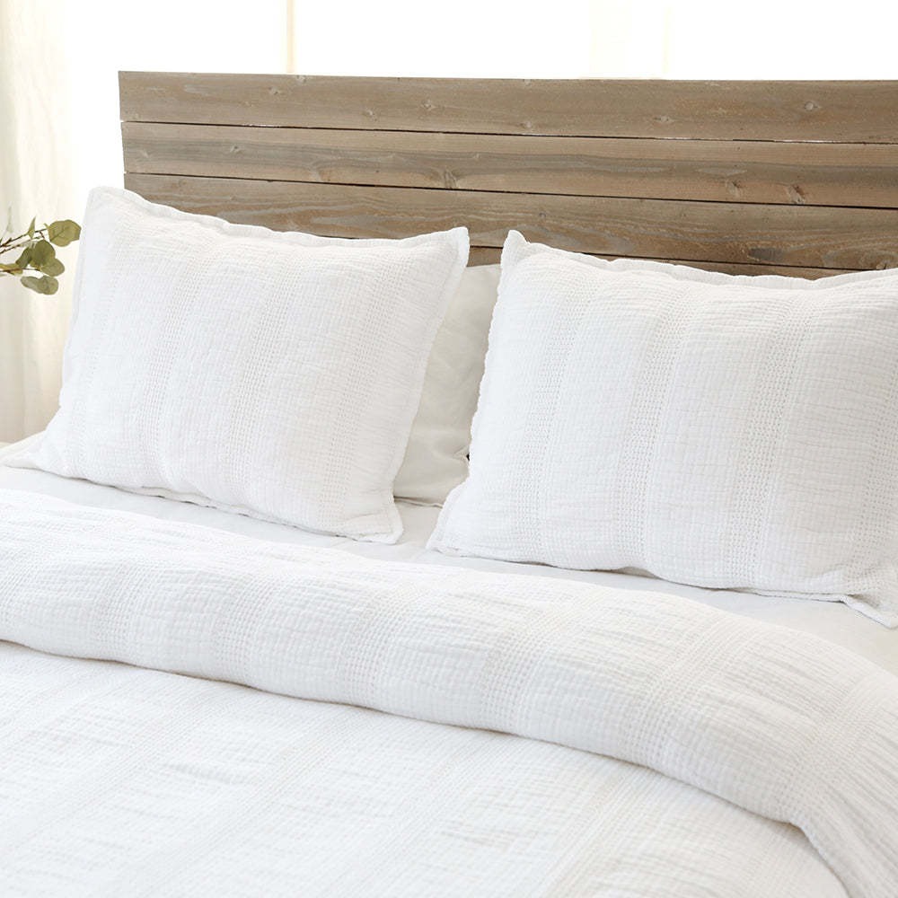a bed with white linens quilt and pillows on top of a wooden headboard
