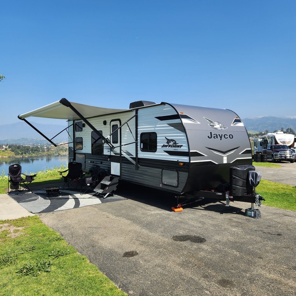 A Jayco Jay Flight travel trailer with an open awning parked at a lakeside RV campsite.