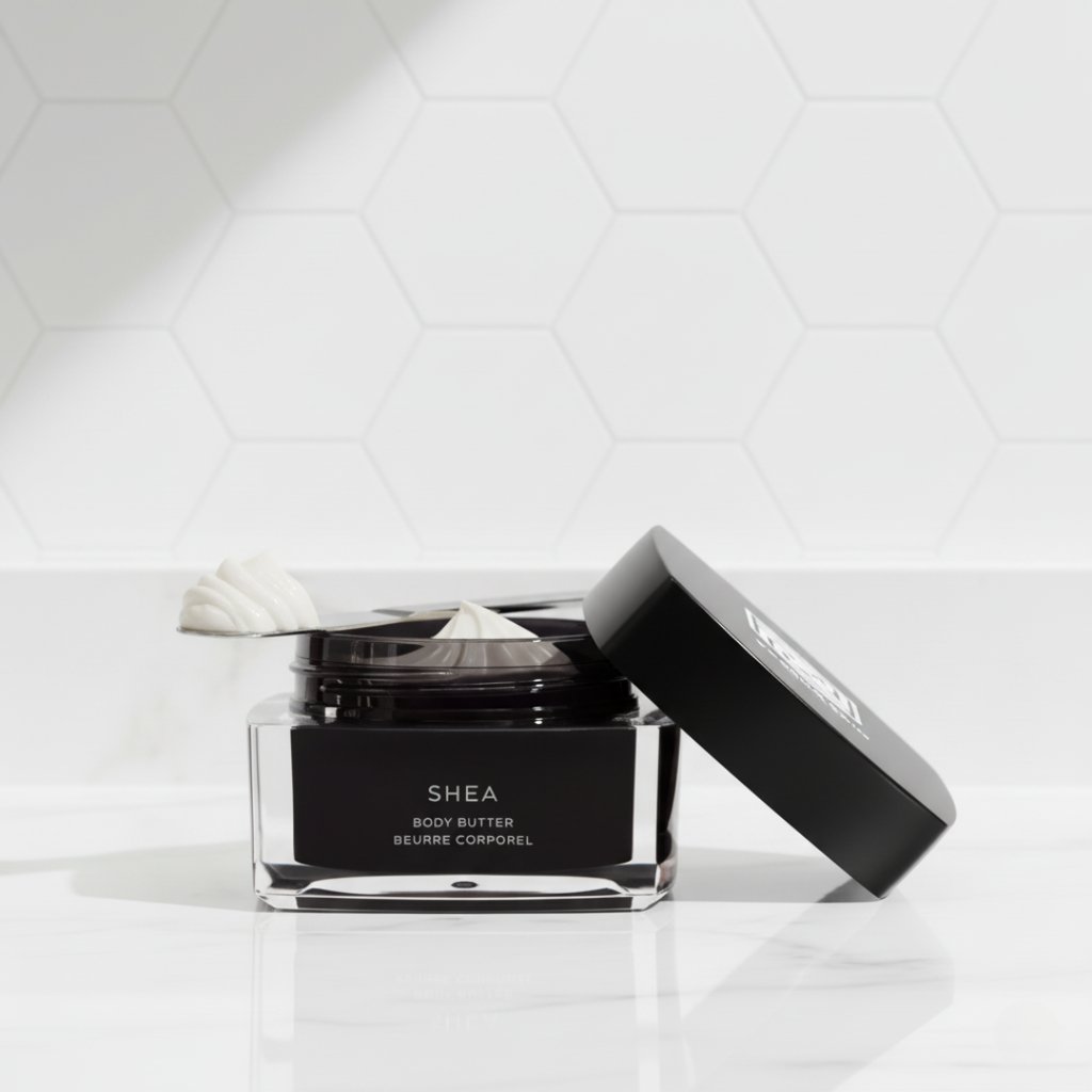 Jar of shea body butter moisturizer on a marble counter with white honeycomb tile background.