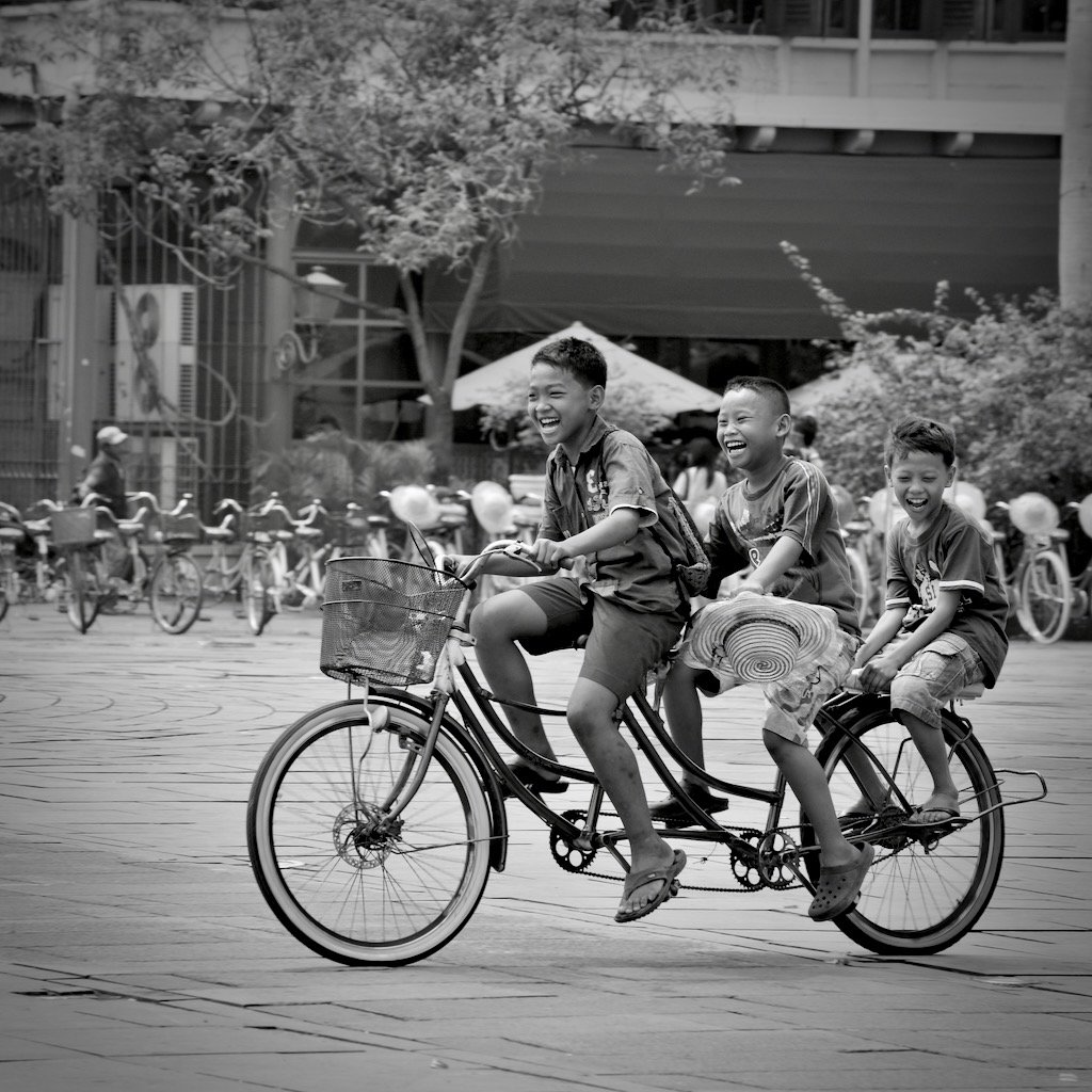 Three joyous youngs Indonesian boys on a bicycle riding in the main square of Kota Tua, Jakarta
