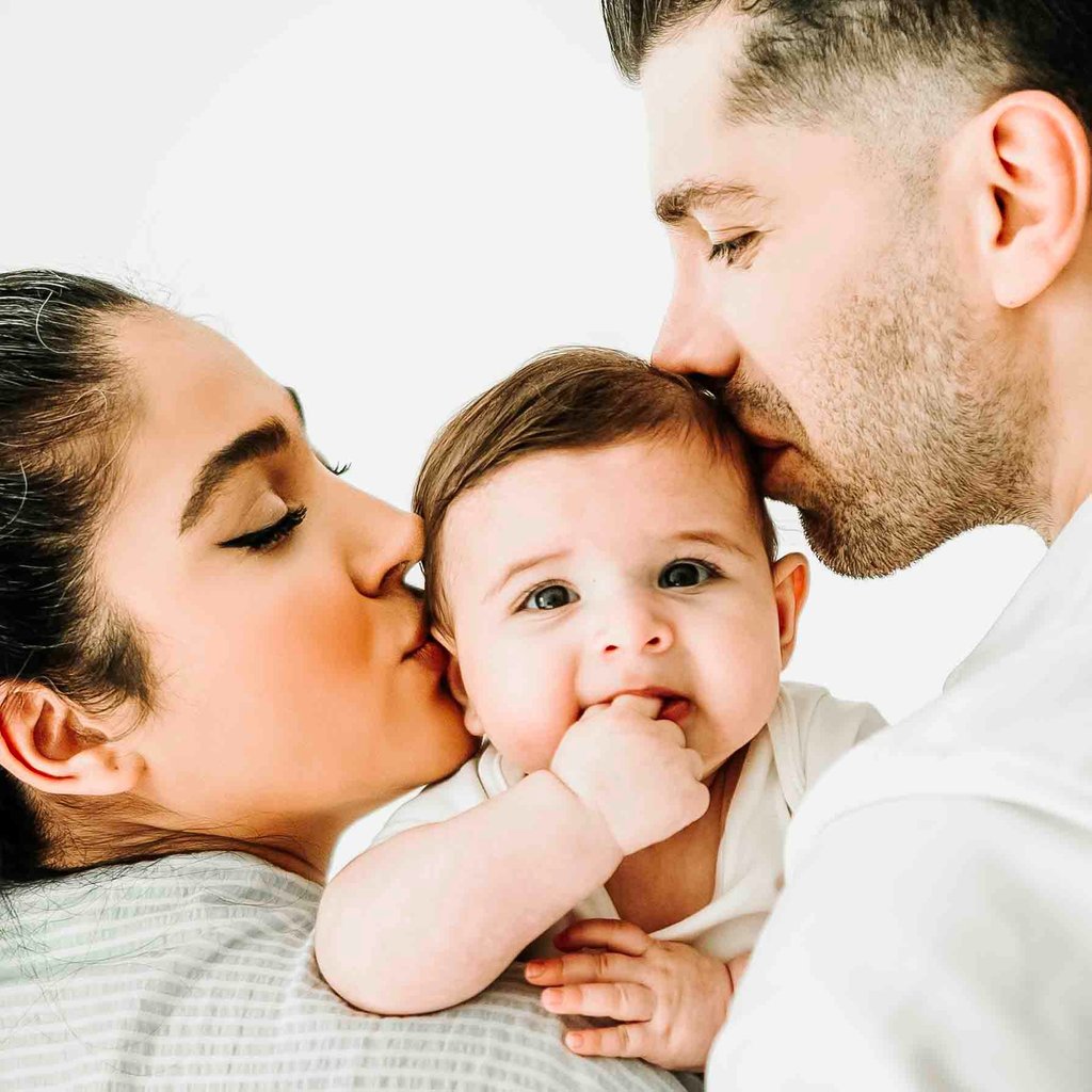 Parents kissing baby during family photoshoot – lifestyle family photography by Fred Art Studio