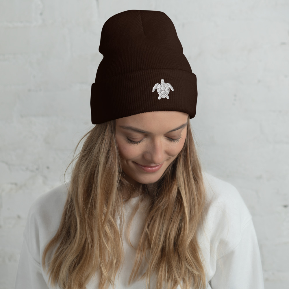 A woman wearing a dark brown cuffed beanie with a white sea turtle embroidery.