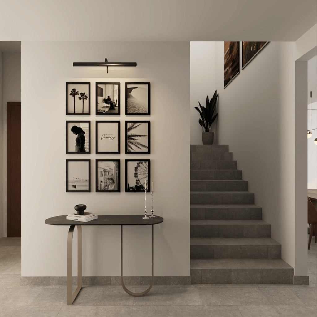 Black and white gallery wall above modern console table in minimal hallway with staircase and plants