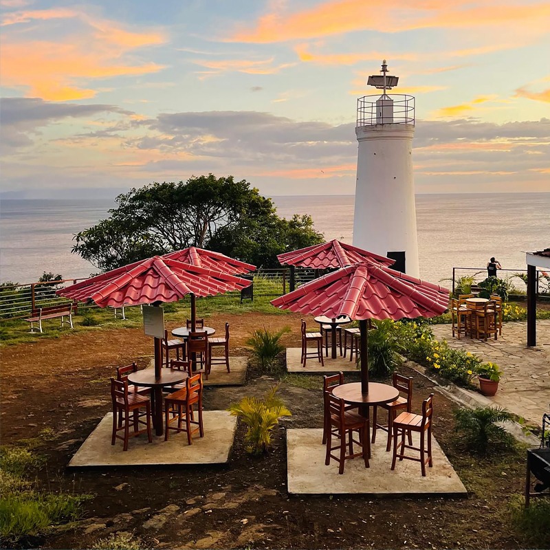 a lighthouse at the top of a hill with tables and umbrellas