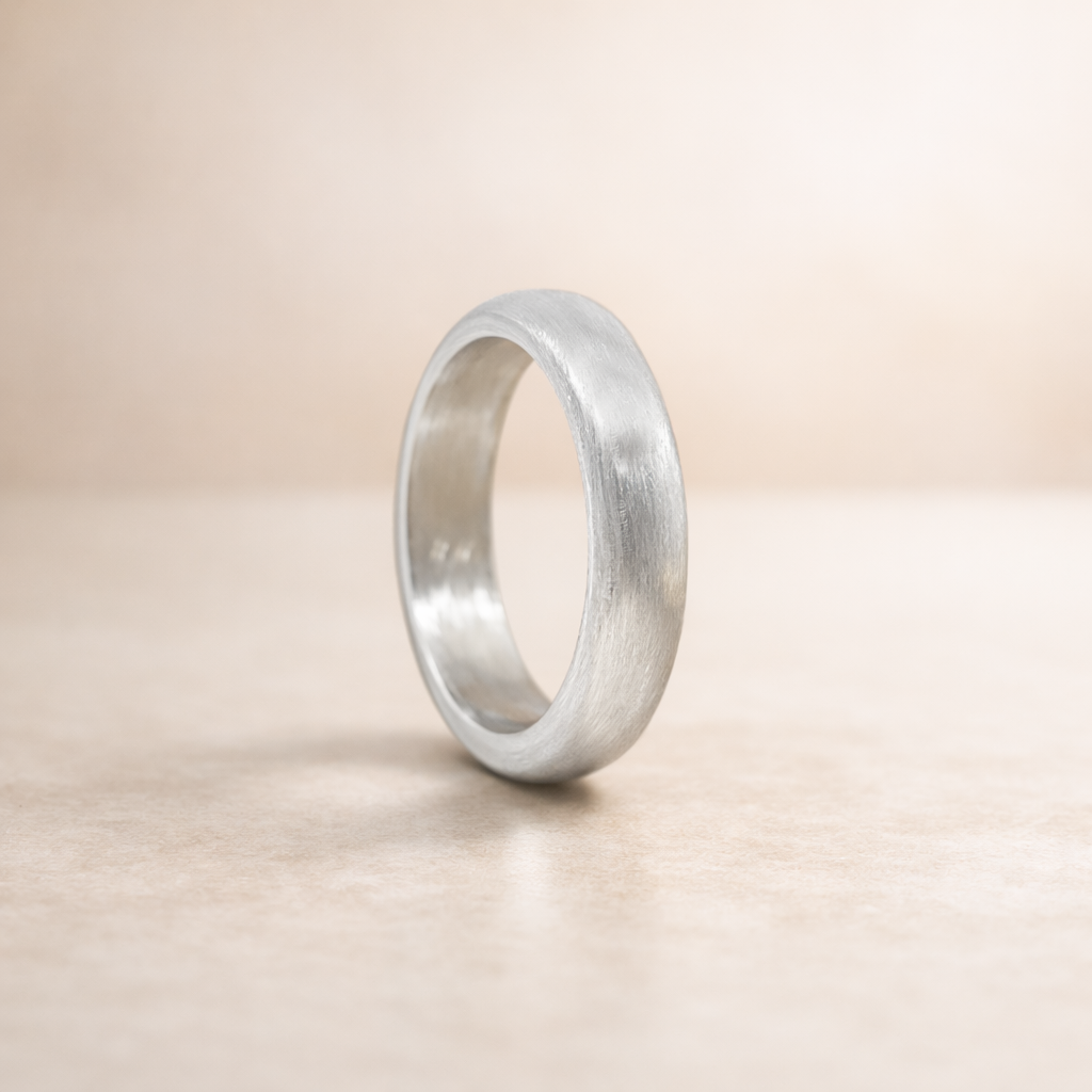 A brushed matte 999 fine silver wedding band standing vertically on a neutral beige background.