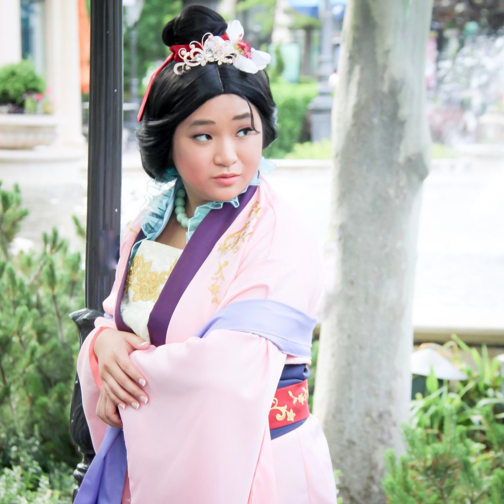 A young woman in a pink and purple Mulan cosplay outfit with traditional Chinese hair accessories.