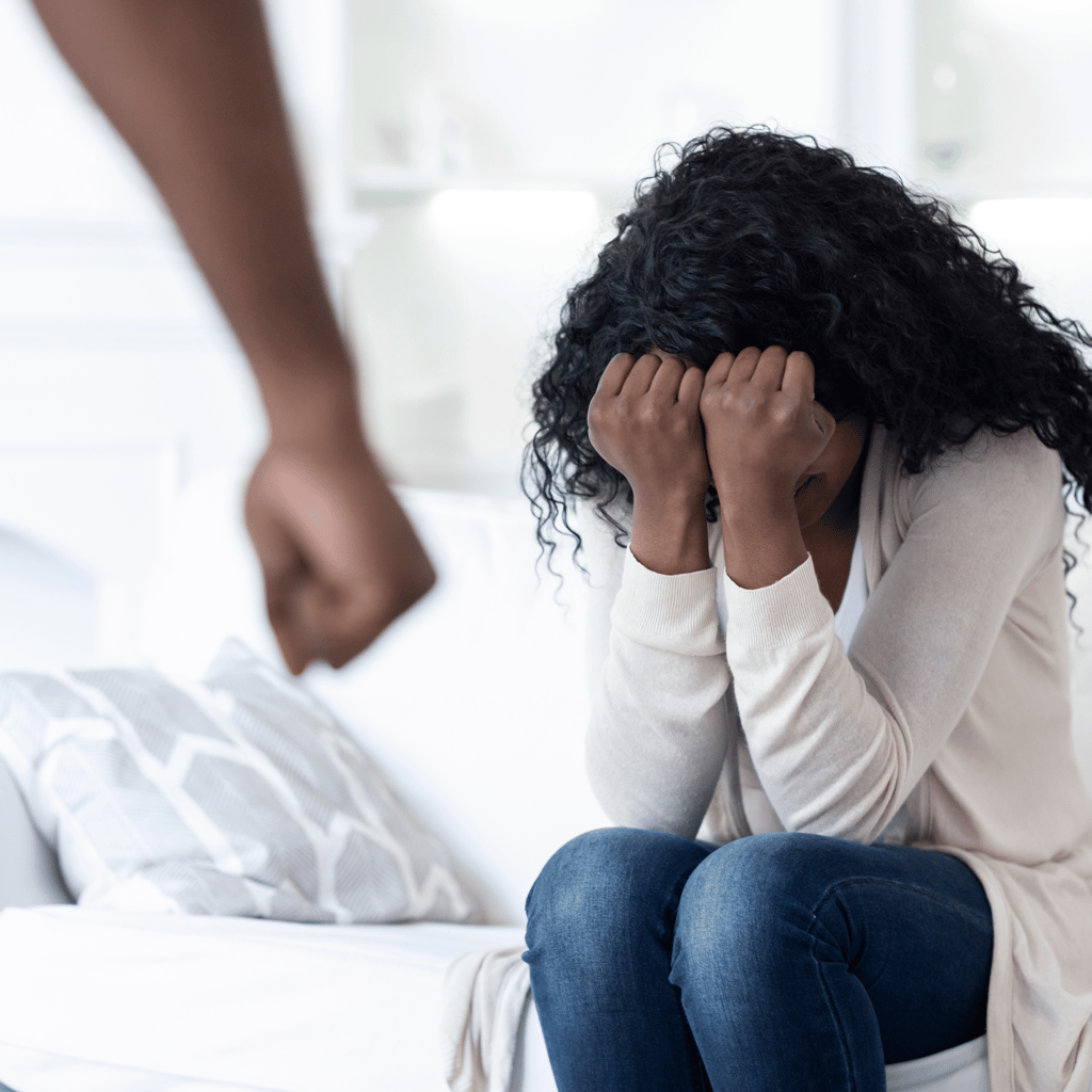 Mujer sentada en su cama abrumada y llorando enfrente de una pareja alterada y agresiva
