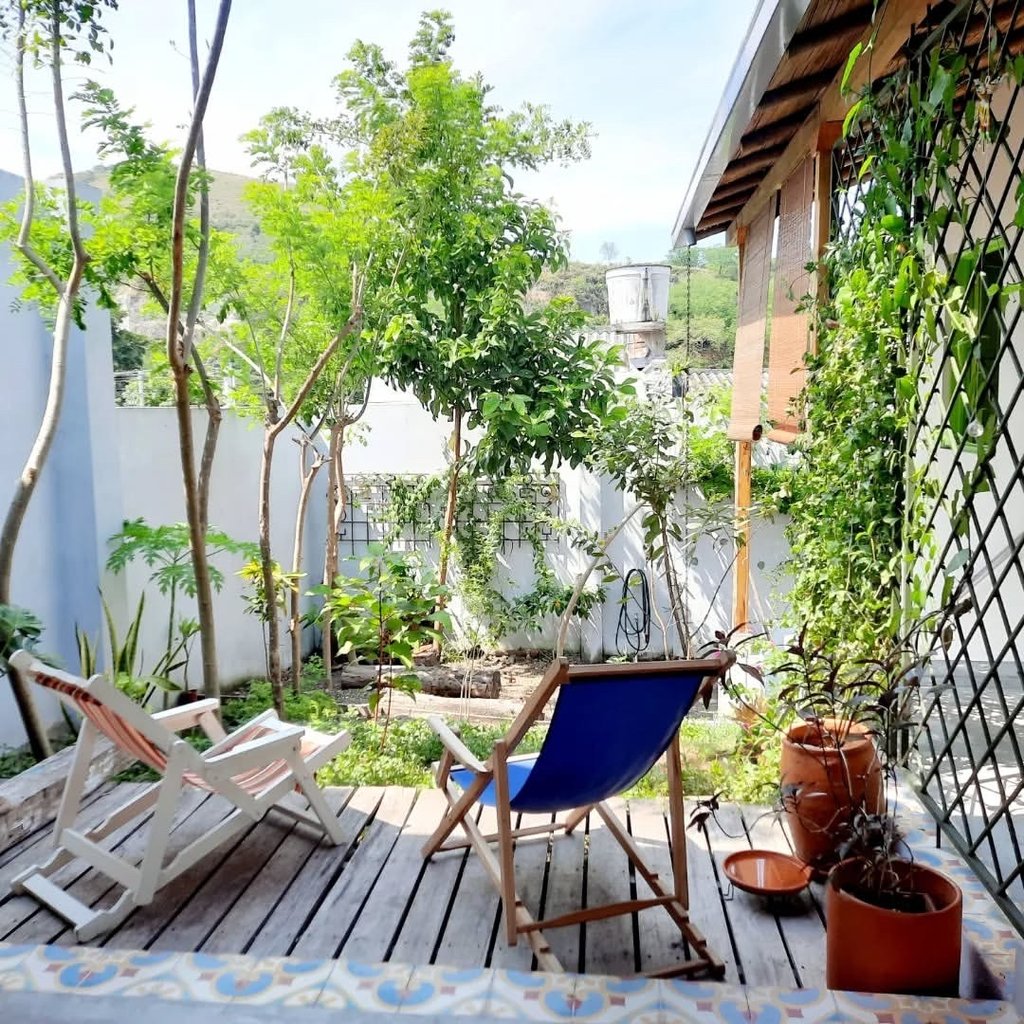 Two folding wooden lounge chairs on a rustic garden deck surrounded by lush green trees and plants.