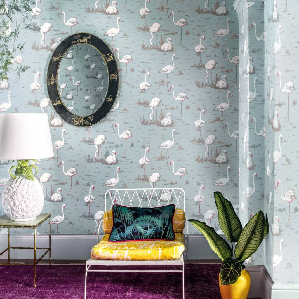 Chic interior featuring pink flamingo wallpaper, a vintage oval mirror, and a tropical lounge chair.