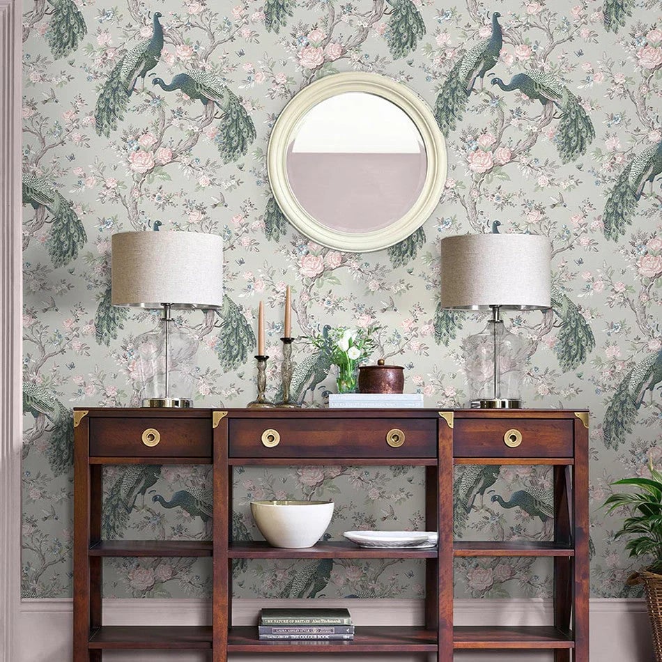 Elegant peacock floral wallpaper behind a dark wood console table with table lamps and a round mirror.