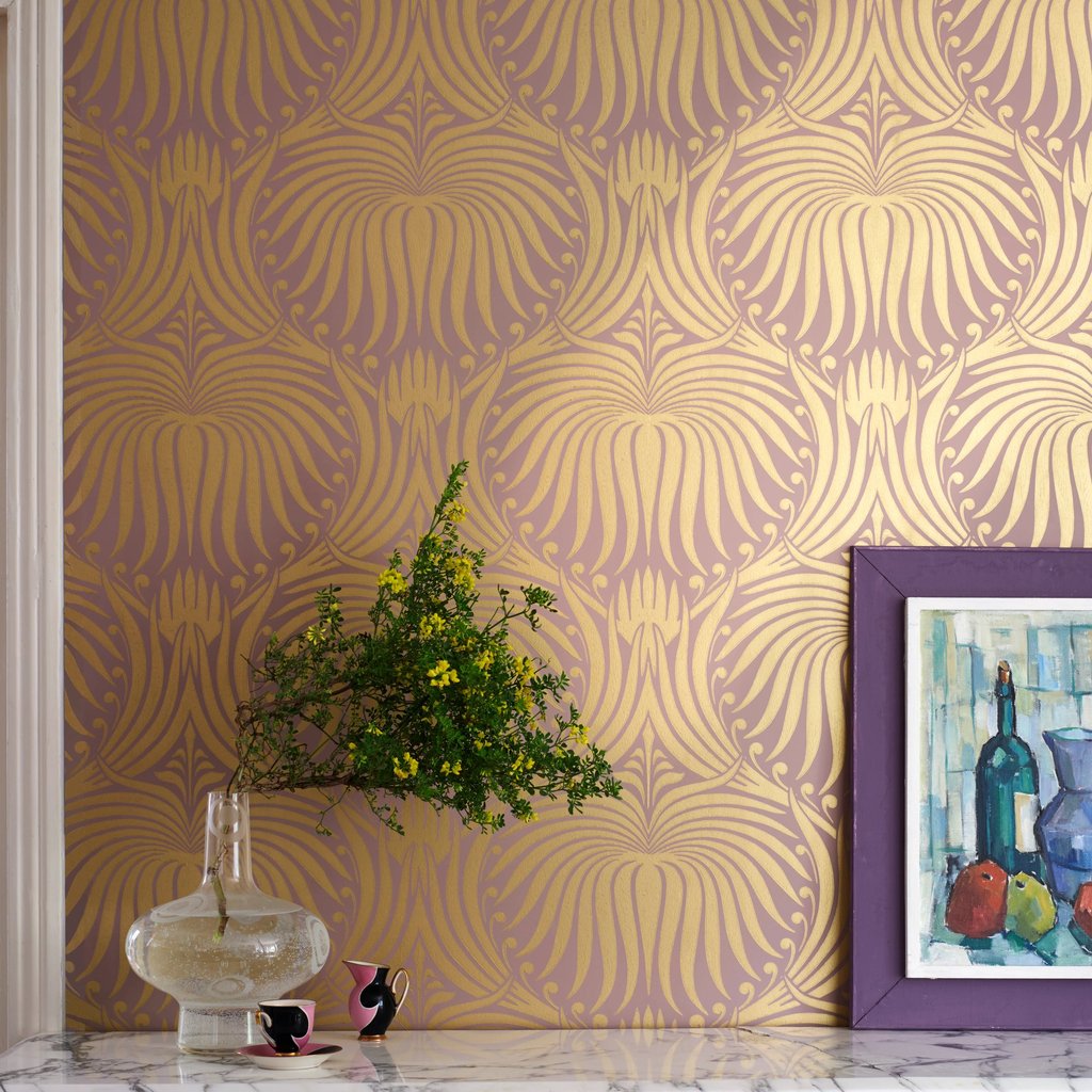 Elegant gold art deco wallpaper pattern behind a marble counter with a glass vase and framed art.