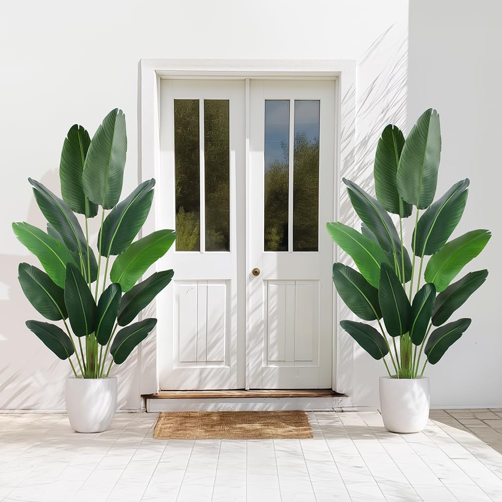 A large artificial bird of paradise plant in white pots flanking a white front door.