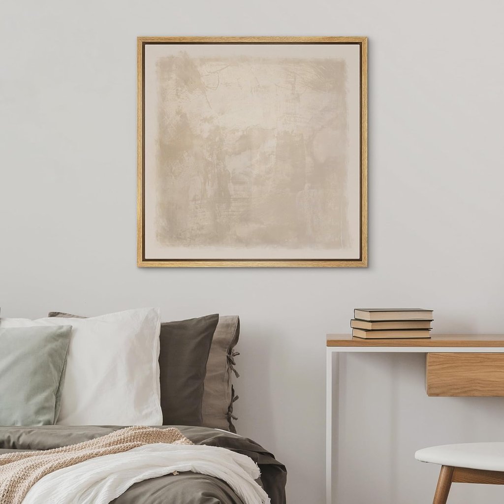 Framed beige abstract wall art hanging above a modern bed and wooden desk in a minimalist bedroom.