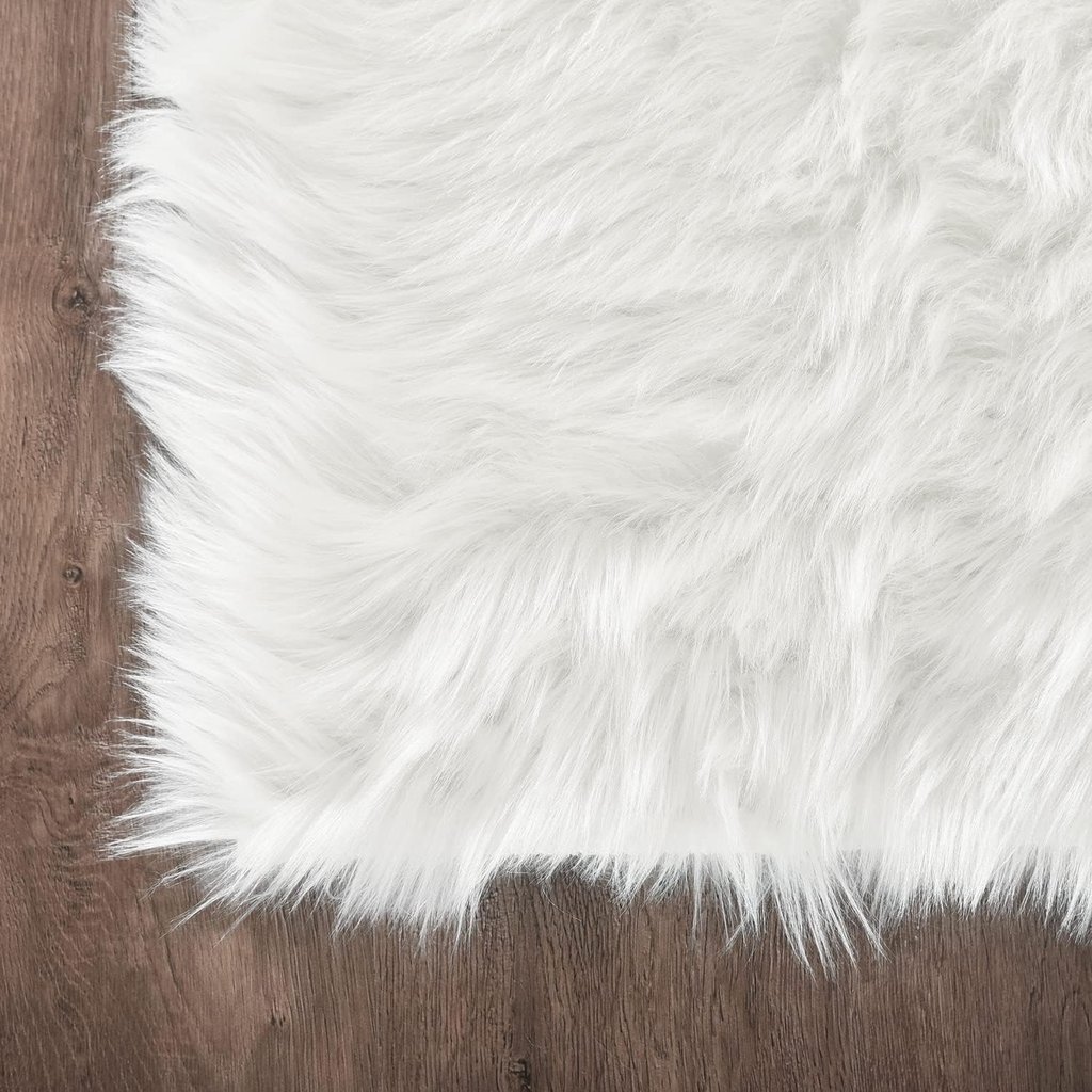 Soft white faux fur rug with shaggy texture placed on a dark brown hardwood floor.