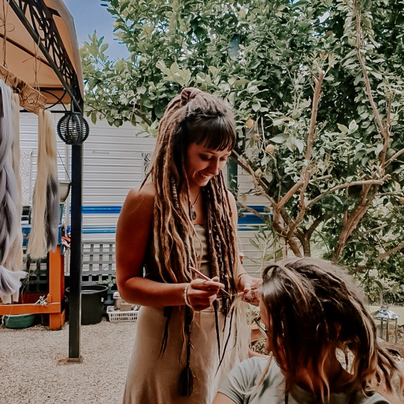 a woman dreadlocking a woman's hair