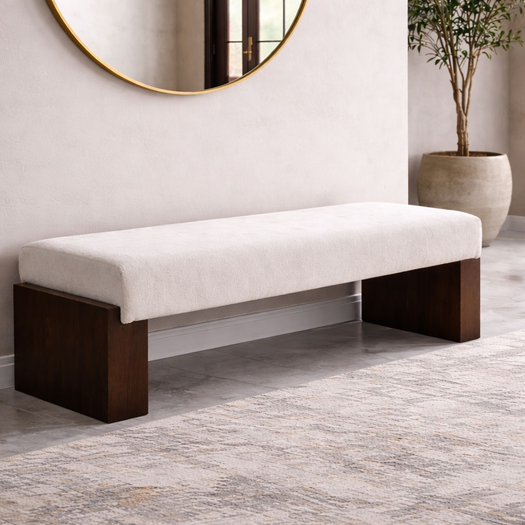 Ivory upholstered bench with dark wood base styled under a round mirror in a minimalist entryway with a neutral rug.