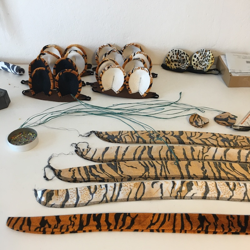 Handmade tiger and leopard animal ear headbands and tails on a white craft table.