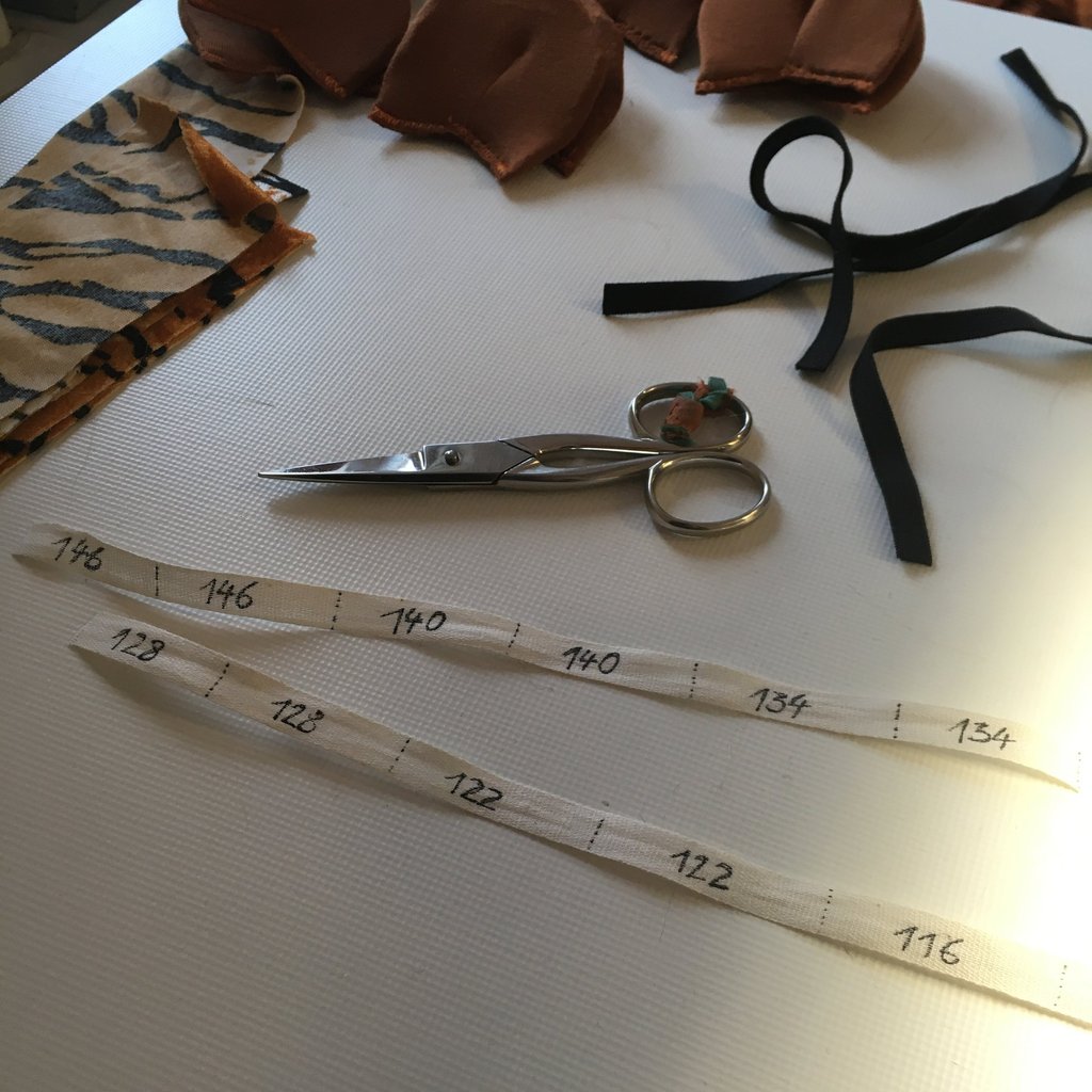 Sewing supplies including sharp scissors, size labels, tiger print fabric, and black elastic ribbon.