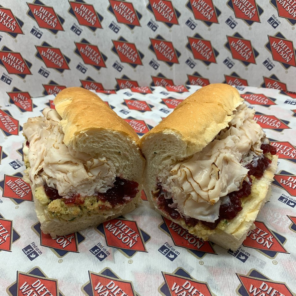A sliced turkey cranberry sub sandwich with stuffing on a hoagie roll with deli branding.