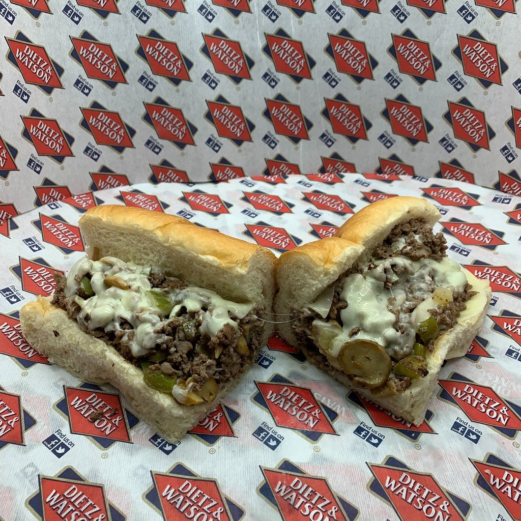 A sliced Philly cheesesteak sandwich with melted white cheese and peppers on Dietz & Watson paper.