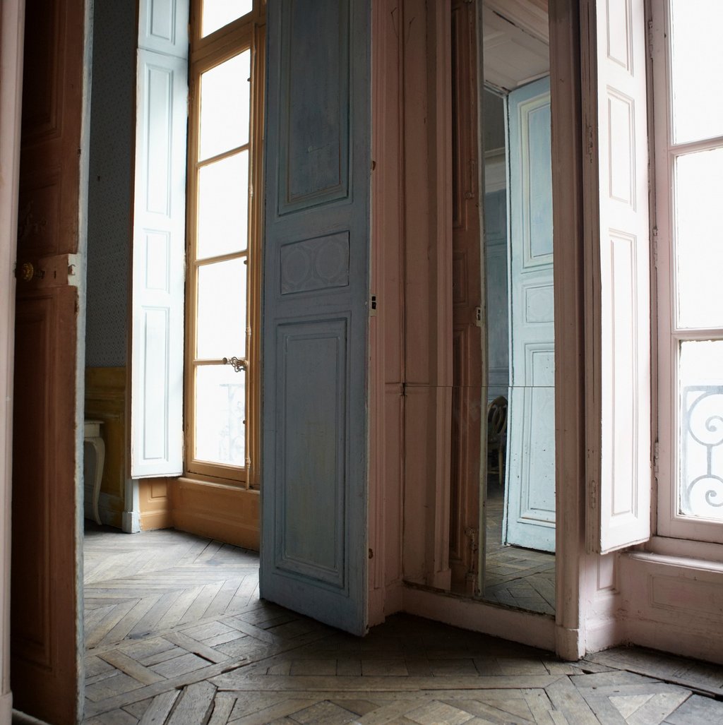 Tall doors standing open in a softly lit Parisian interior, with natural light streaming across aged