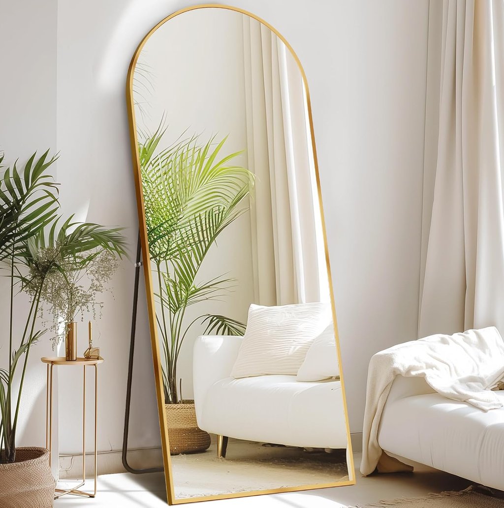 Gold arched full length floor mirror leaning against a white wall in a modern living room.