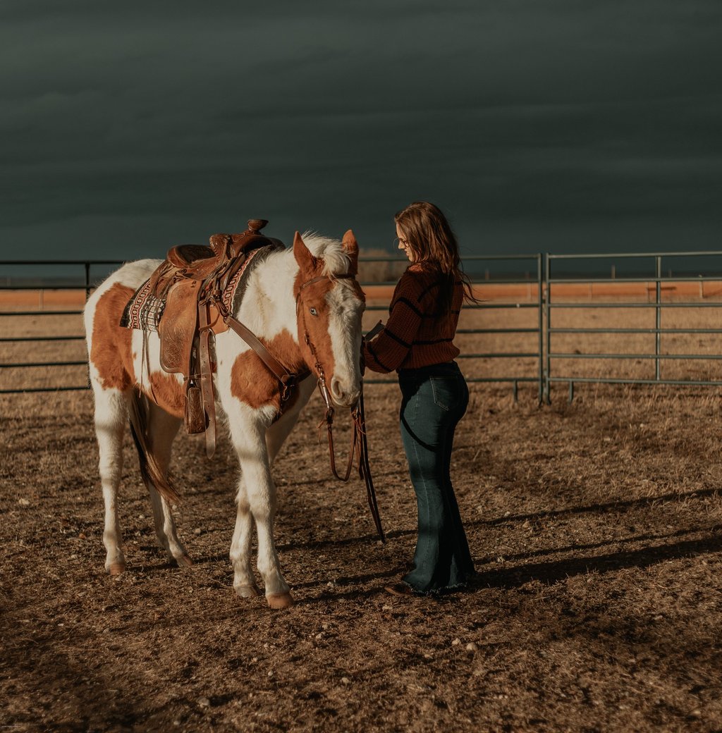 a woman is saddling a paint horse