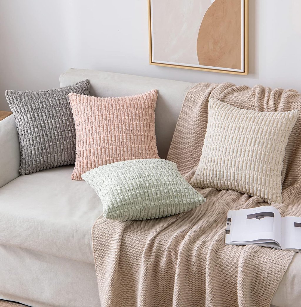 Decorative ribbed corduroy throw pillows in pastel colors arranged on a white sofa with a beige knit blanket.