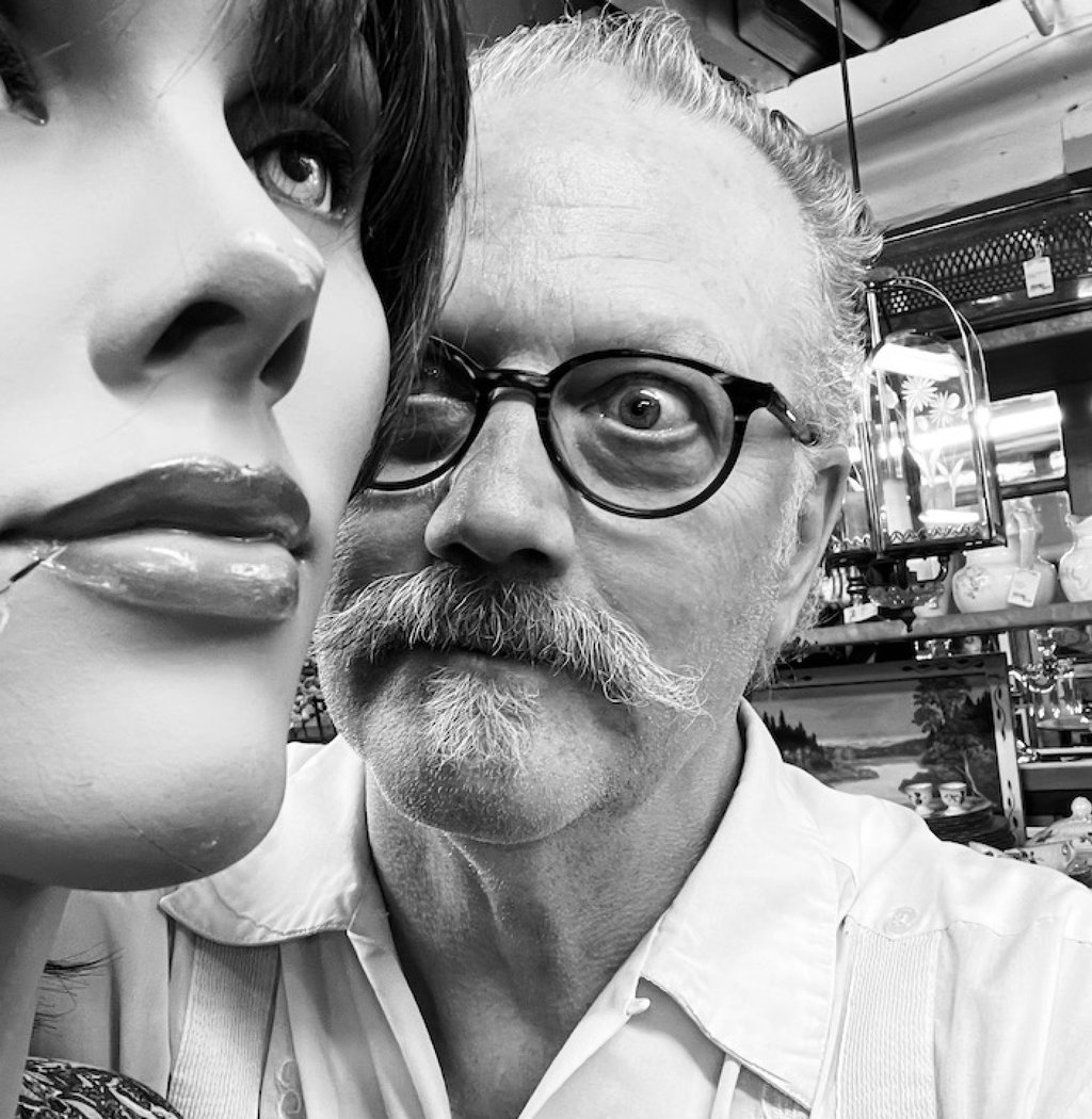 Dan Self, a man with a mustache and glasses looking at a mannequin