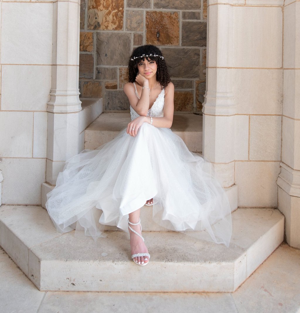 quinceanera in a white dress sitting on a stone stepstone