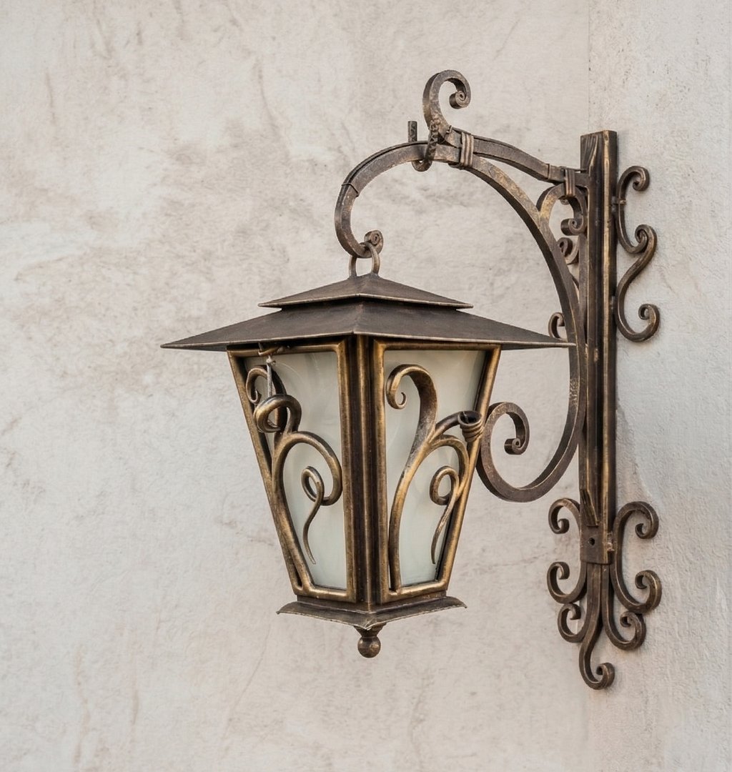 Vintage bronze outdoor wall lantern with ornate scrollwork on a textured stone wall.