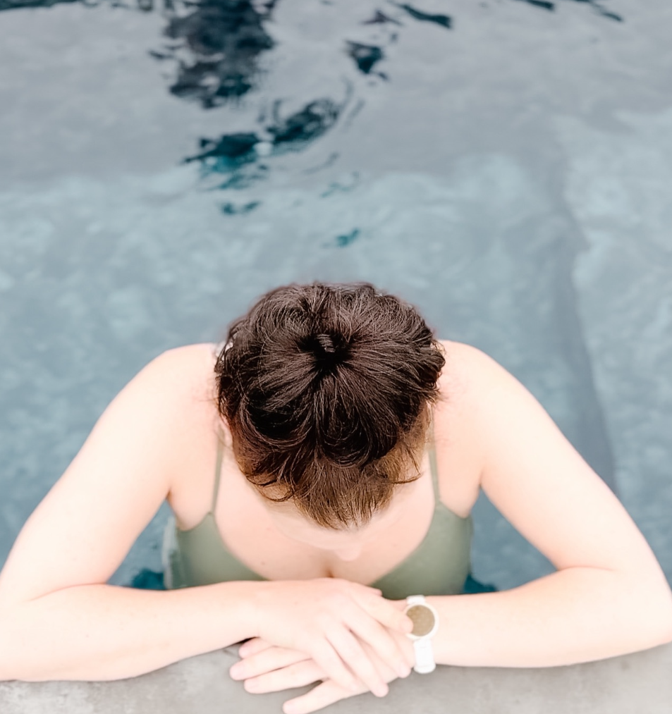 A woman in a green swimsuit resting her arms on the edge of a cold plunge pool at Saltair Nordic Spa