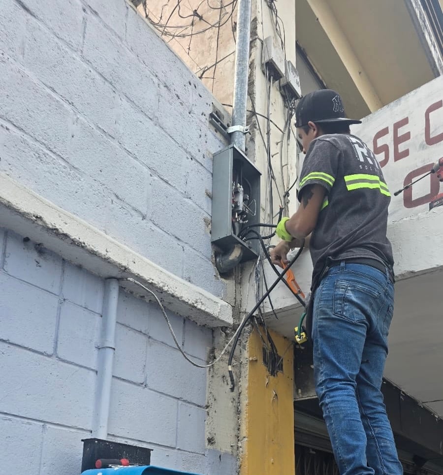 Instalación eléctrica en acometida de edificio por técnico con uniforme.