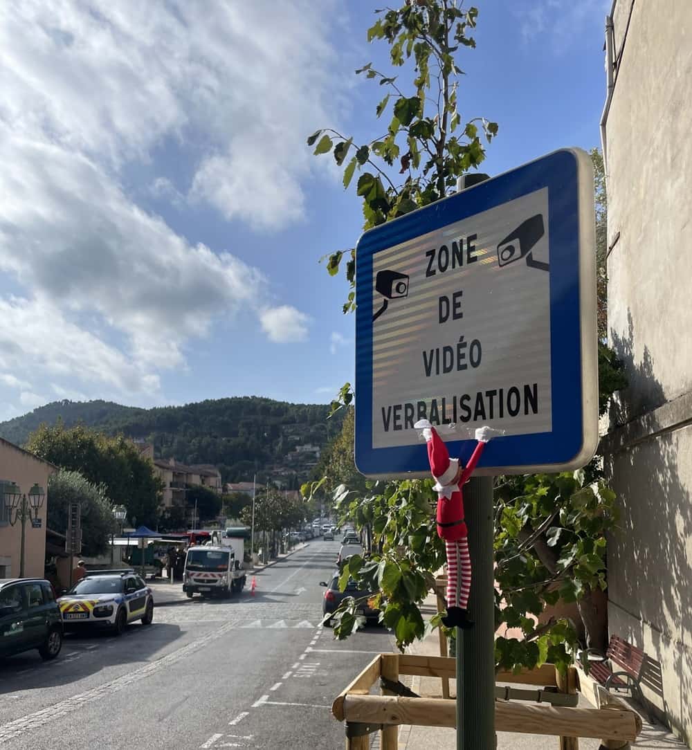 photo d’un lutin farceur accroché à un panneau en ville, tradition de Noël
